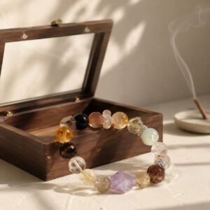 Macro close-up of a curated good luck charm bracelet showcasing natural translucent amethyst, clear crystal, green phantom, and rose quartz beads, nestled gently inside an unvarnished natural wooden box under soft, dappled forest light.