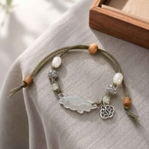 Close-up of a handcrafted natural jade feng shui bracelet featuring an intricately carved lotus flower charm, 24h sound-bath calibrated at 528Hz for 2026 emotional balance, nested inside a signature white Luxe Abundance Box.